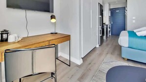 Ein modernes Hotelzimmer mit Fernseher, einem Holztisch mit Stuhl, einem Bett mit blauer und weißer Bettdecke und einer Tür zum Badezimmer.