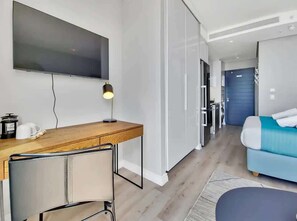 A modern hotel room with a flat-screen TV, a wooden desk with a chair, a bed with a blue and white duvet, and a door leading to the bathroom. - Paradise views: Couples sanctuary w/ pool, parking (Cape Town)