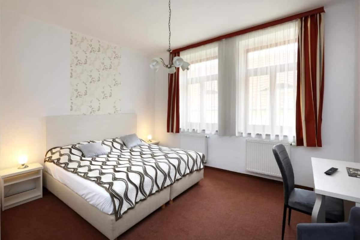 A bedroom with a bed, bedside tables, a desk, and a chair.