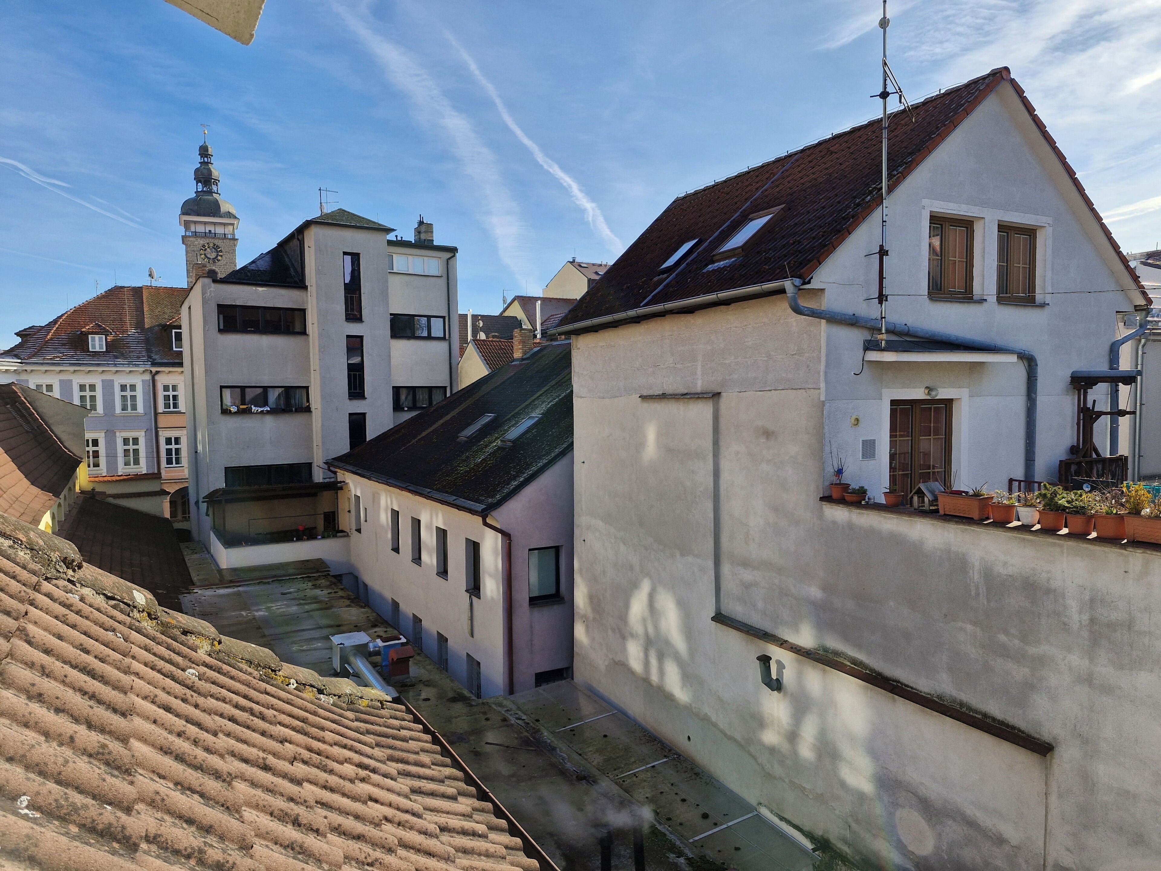 A narrow urban street with buildings, a clock tower, and a clear sky.