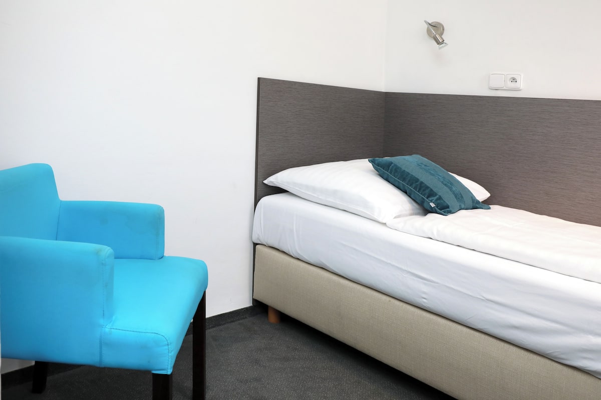 A room with a bed, a blue chair, and a wall socket.