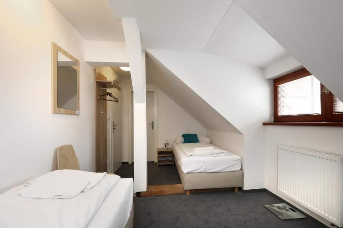 A small, compact room with a bed, a chair, a mirror, and a window.