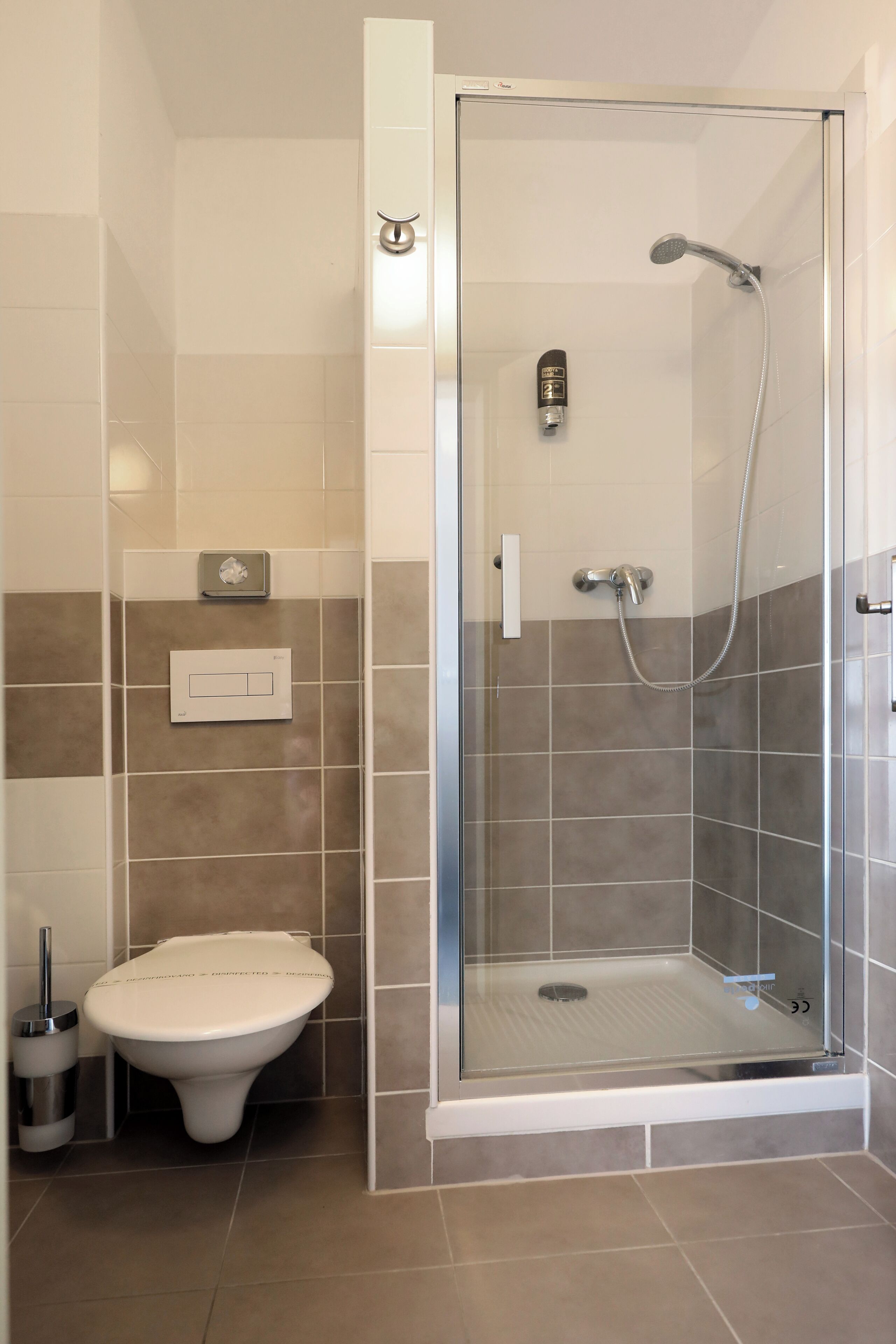 Un baño moderno con ducha de vidrio, inodoro y dispensador de jabón en la pared.
