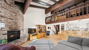 Uma sala de estar com lareira, estantes de madeira, uma televis ão e uma área de jantar com cadeiras de madeira e uma escada.