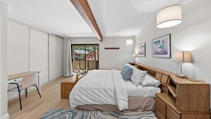 Quarto com cama, mesas de cabeceira, escrivaninha e janela.