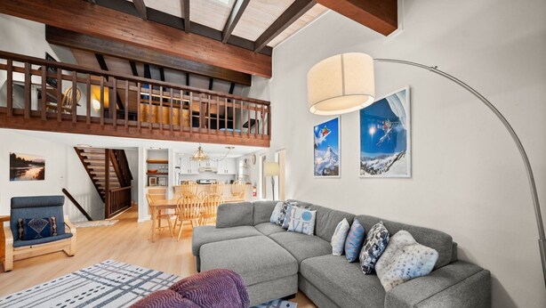 Uma sala espaçosa com um sofá seccional cinza, uma escada de madeira e uma área de jantar.