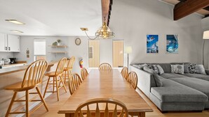 Uma cozinha moderna com armários de madeira, uma mesa de jantar com cadeiras, um sofá cinza e duas pinturas penduradas na parede.