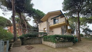 Un bâtiment à deux étages doté d’un balcon, d’un escalier et d’une zone pavée agrémentée d’arbres et d’arbustes.