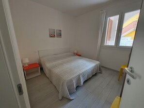 A bedroom with a bed, nightstands, a window, and a door.