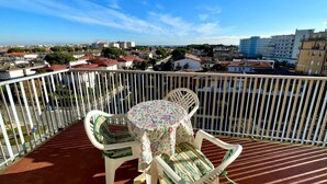 En balkon med et bord og stole, udsigt over et bybillede med bygninger og en klar himmel.