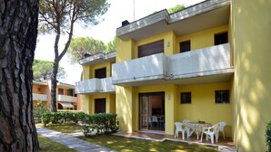 A yellow building with a balcony, a table with chairs, and a small garden area. - Perfect flat with garden and pool access (Bibione)