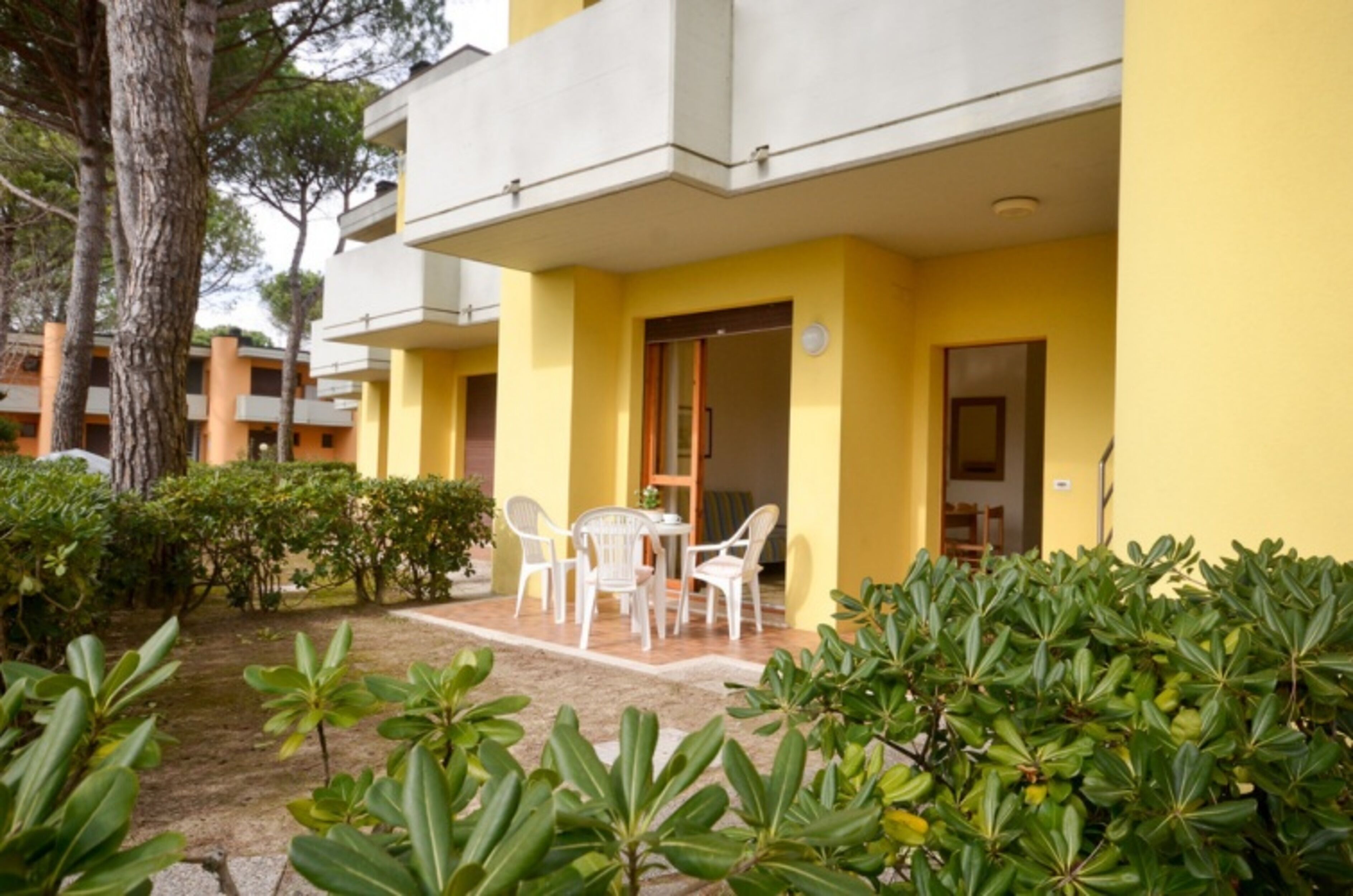 A yellow building with a balcony, white chairs, and a small table.