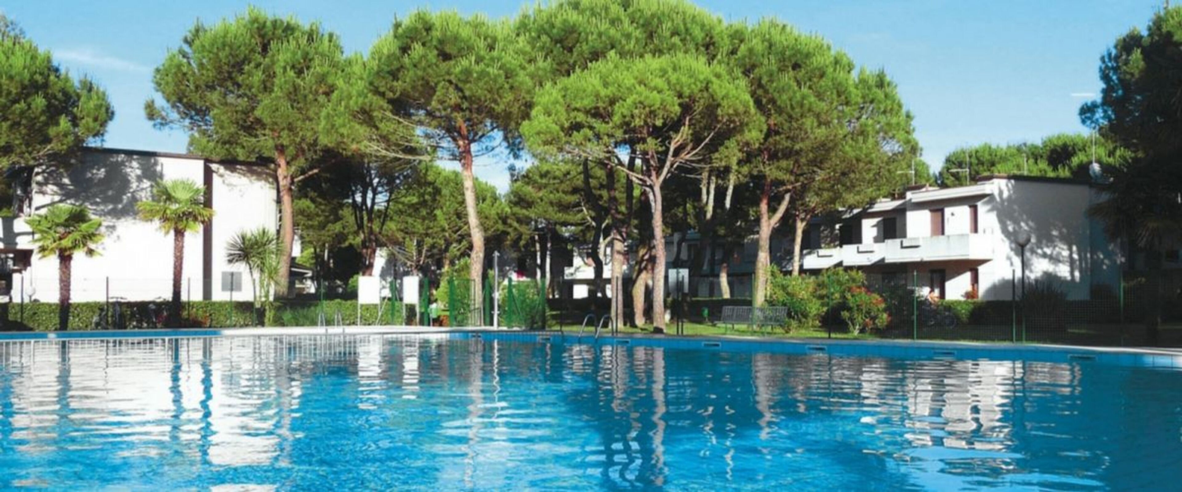 Ein Schwimmbecken mit klarer, blauer Wasseroberfläche, umgeben von Bäumen und Gebäuden.