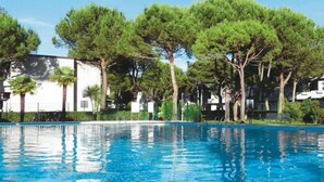 A swimming pool with a clear blue water surface, surrounded by trees and buildings. - Perfect flat with garden and pool access (Bibione)