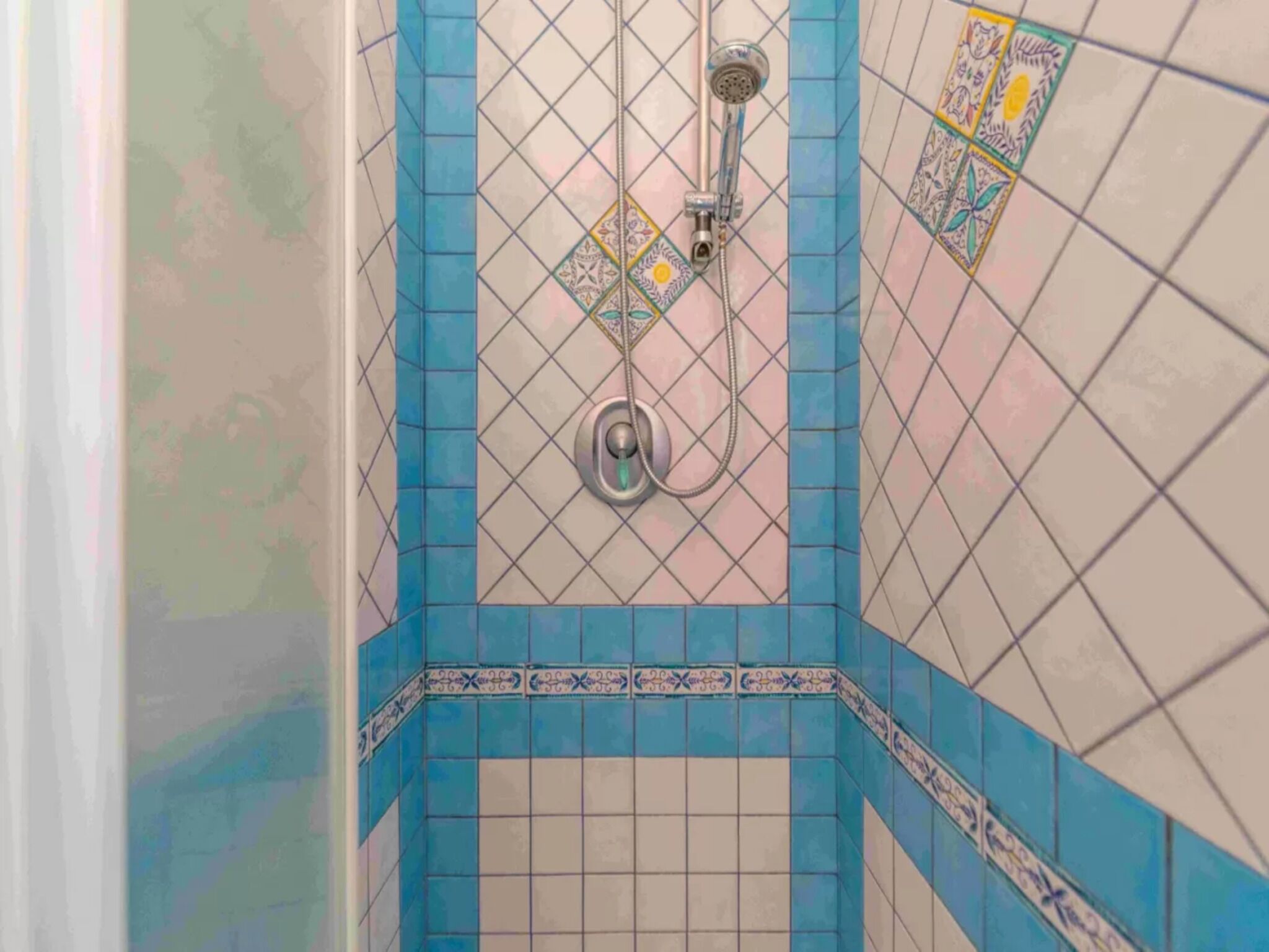 A bathroom with blue and white tiles, a shower with a handheld showerhead, and a wall-mounted faucet.