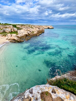 Un paisaje costero con aguas turquesas cristalinas, formaciones rocosas y una playa arenosa.