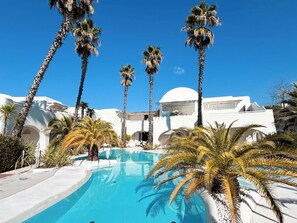 Ein Pool, umgeben von Palmen und weißen Gebäuden mit Bögen.