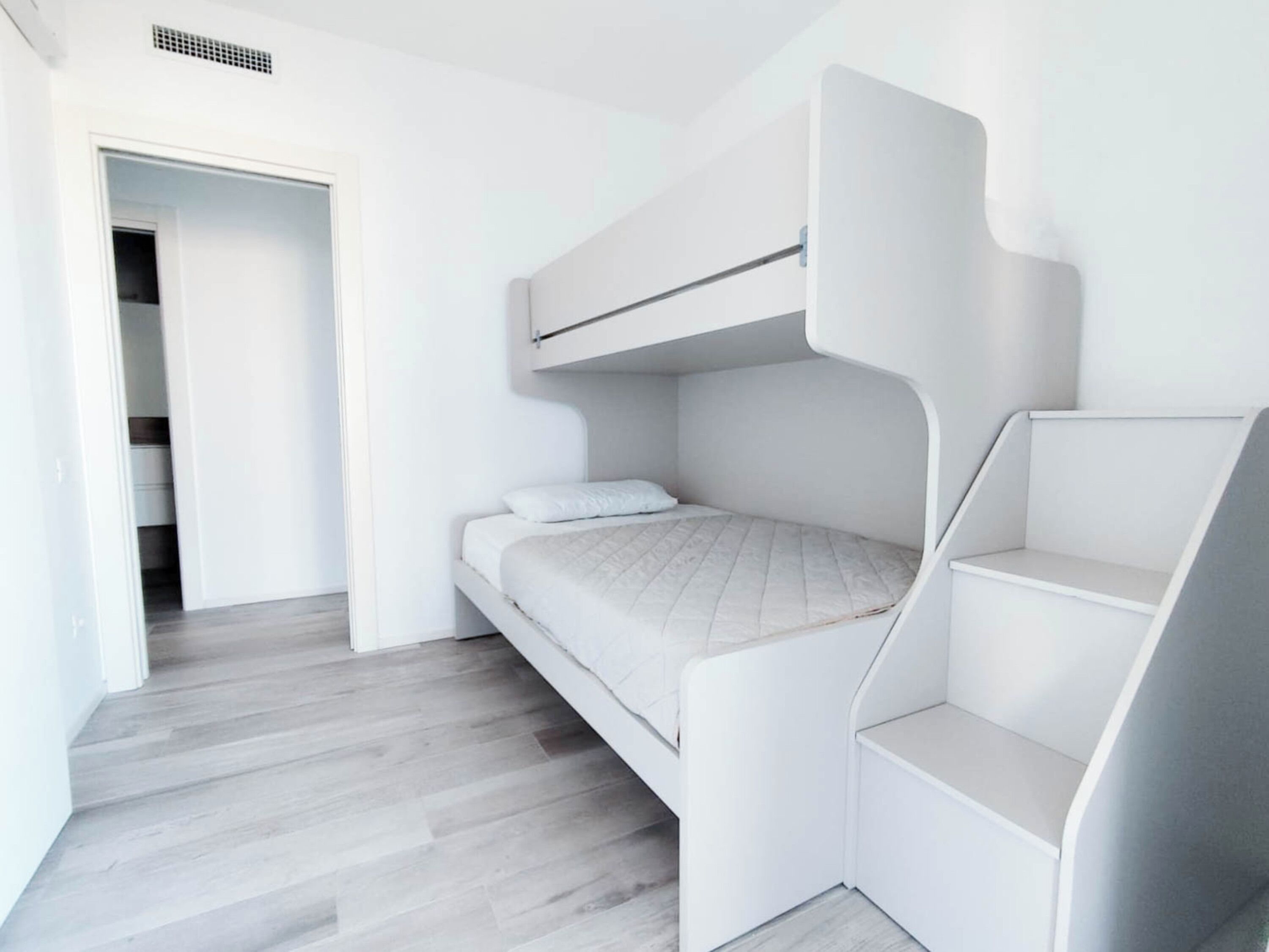 A bunk bed room with a white color scheme, a door leading to a closet, and a wooden floor.