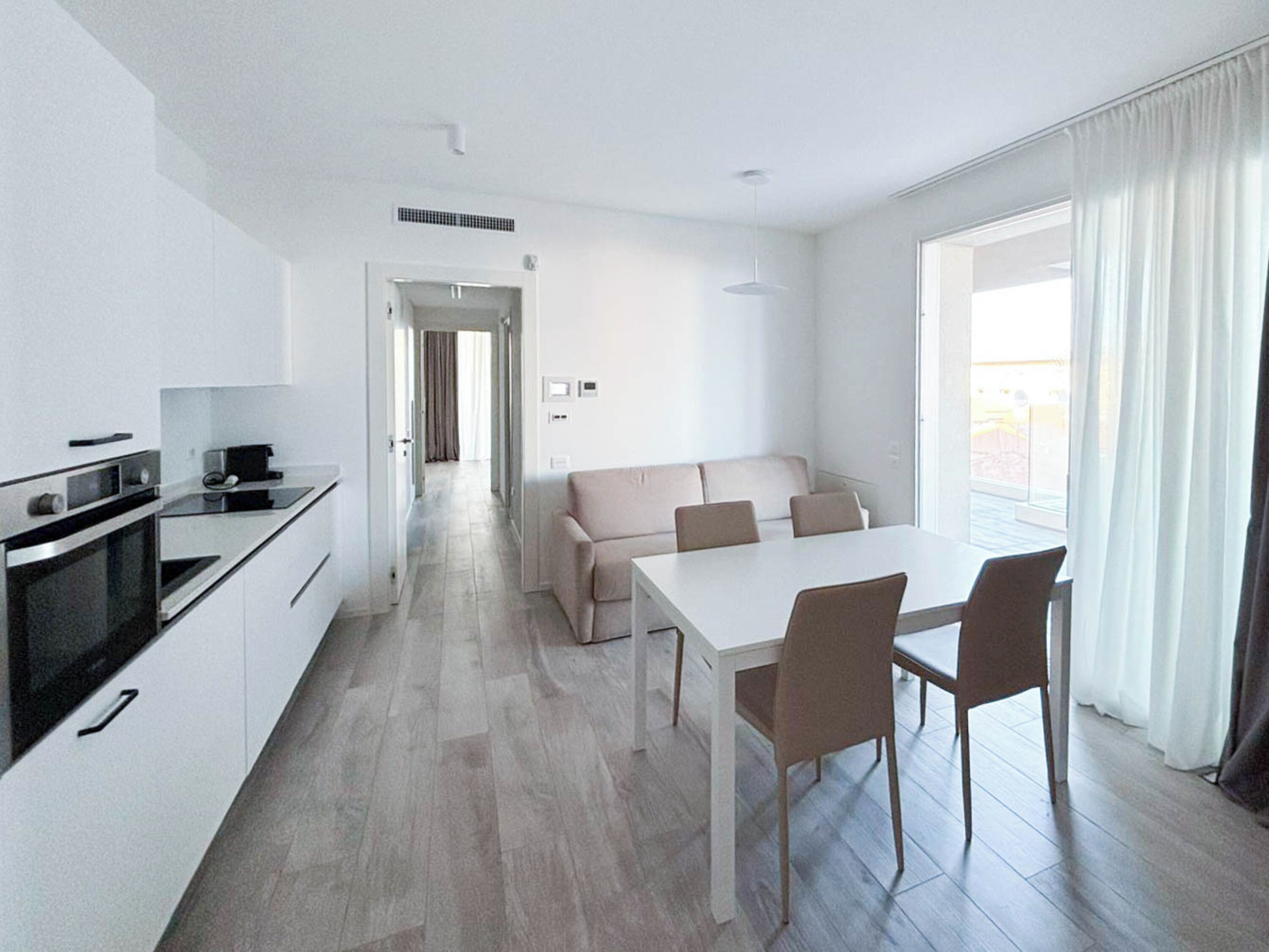 A modern kitchen with a dining area, a sofa, and a large window.