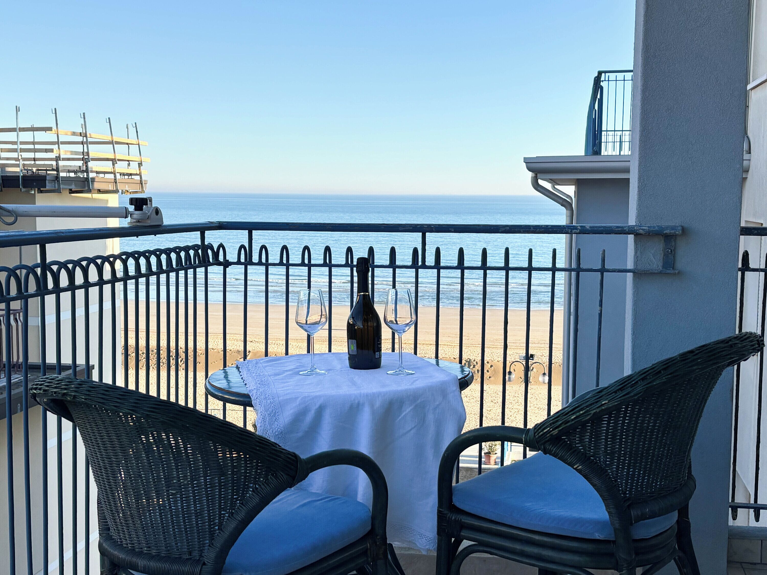En balkon med et bord, to stole, en flaske og et glas.