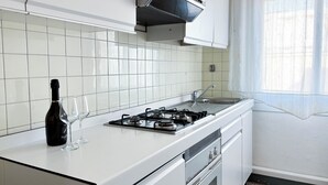 Una cocina con armarios blancos, una estufa a gas, un fregadero y un ventanal con cortinas.