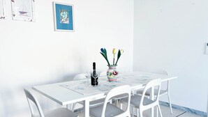 Una mesa de comedor blanca con cuatro sillas, una botella de vino y un florero con flores.