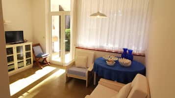 Un salon comprenant une télévision, un canapé, une table à manger recouverte d’une nappe bleue et une chaise.