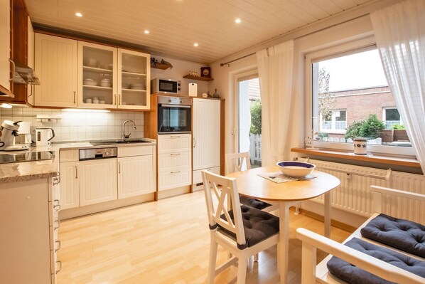 A kitchen with white cabinets, a microwave, and a stove. There is a dining table with chairs and a bowl on it. - Villa Wicking - Right on the South Beach - Beautiful family apartment (Borkum)