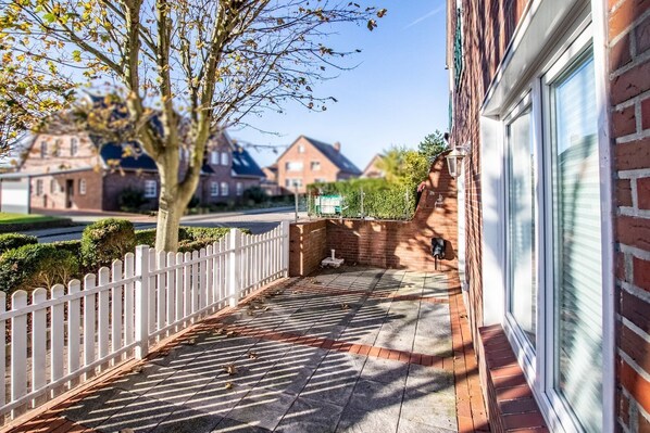En bostadsfastighet med en asfalterad uppfart, ett vitt staket och ett hus i tegel med ett stort fönster.