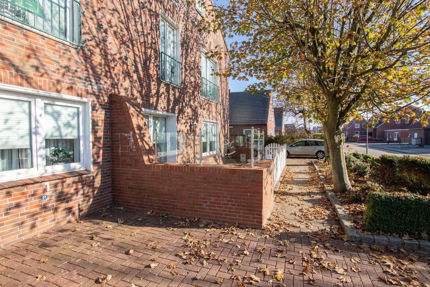 A brick building with a paved driveway, a tree, and a parked car.