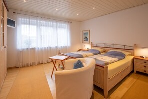 A bedroom with a bed, bedside tables, a chair, a window with curtains, and a wall-mounted TV. - Villa Wicking - Right on the South Beach - Beautiful family apartment (Borkum)