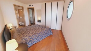 A bedroom with a bed, a bedside table, a lamp, a mirror, and a wardrobe. - Modern flat with panoramic view (Lignano Sabbiadoro)