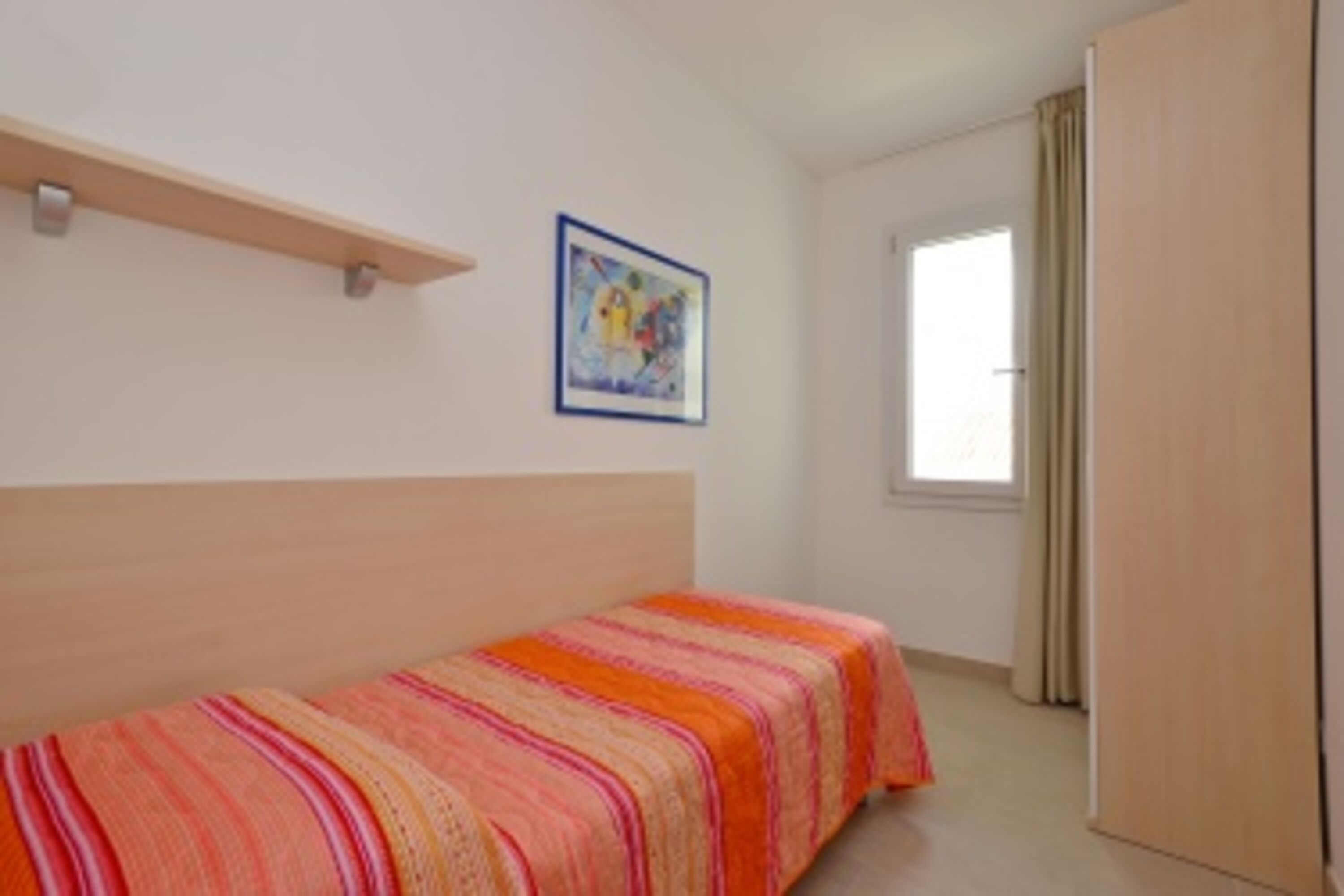 A room with a bed, a painting on the wall, a window with curtains, and a wardrobe.
