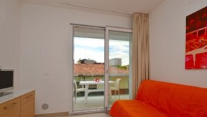 Ein Schlafzimmer mit einem Bett, einem Fernseher auf einer Holzkommode und einer Glastür, die zu einem Außenbereich mit Tisch und Stühlen führt.