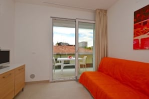 A bedroom with a bed, a TV on a wooden dresser, and a sliding glass door leading to an outdoor area with a table and chairs. - Delightful apartment with pool (Lignano Sabbiadoro)