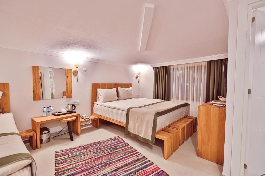 A hotel room with a bed, bedside table, desk, and a colorful rug.