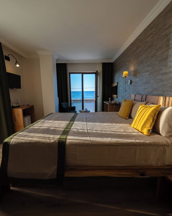 A hotel room with a large bed, a desk, a chair, a television, and a view of the ocean through the door. - Livadi Jur  (Akcakoca)