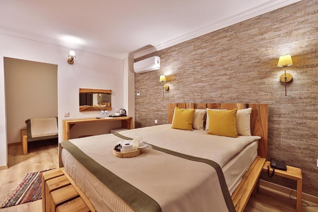 A hotel room with a bed, bedside table, lamp, and a small desk with a chair.