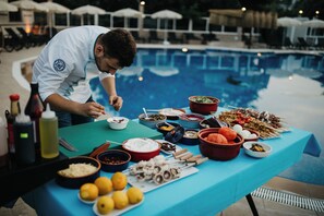 Un buffet installé au bord de la piscine, proposant divers plats, et une personne qui sert les clients.