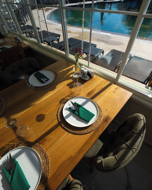 A dining area with tables set for two, a view of a pool outside, and a window overlooking the pool area.