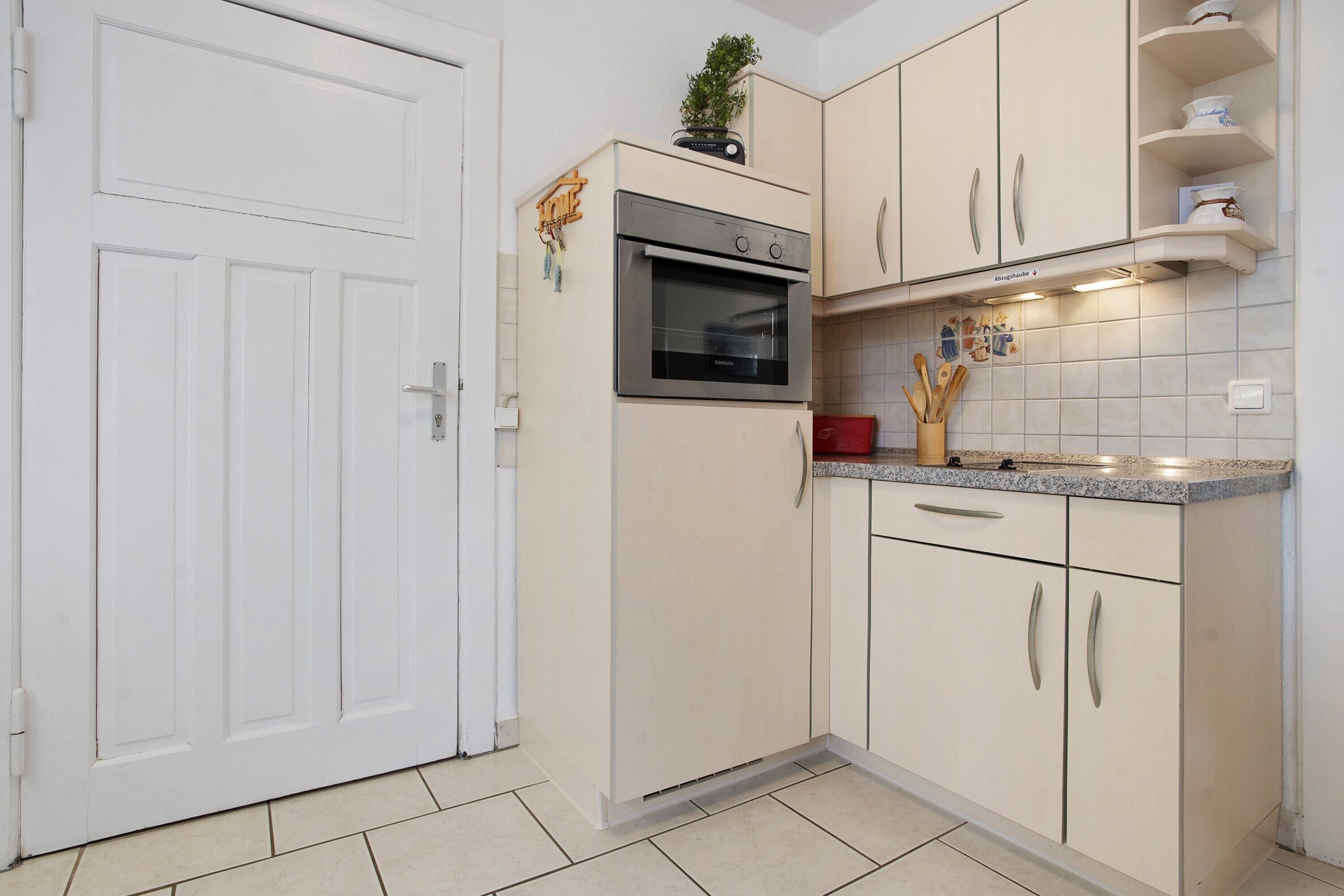 A kitchen with a white door, a built-in oven, and a countertop with utensils.