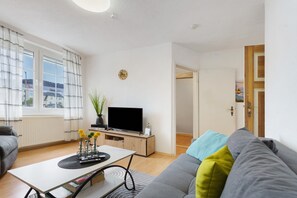 Ein Wohnzimmer mit einer Couch, einem Couchtisch, einem Fernseher und einem Fenster mit Vorhängen.