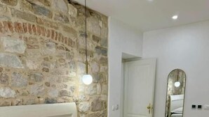 Une chambre d’hôtel avec un mur en pierre, un lit avec du linge de lit blanc, un miroir rond et une porte.