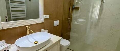 A modern bathroom with a large mirror, a round sink, a toilet, and a glass-enclosed shower.