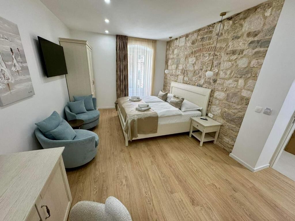 Un dormitorio con cama, dos mesitas de noche, televisor, silla y pared de piedra.