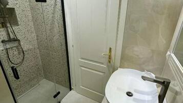 Un baño con cabina de ducha de vidrio, una puerta blanca y un lavabo redondo con grifo.
