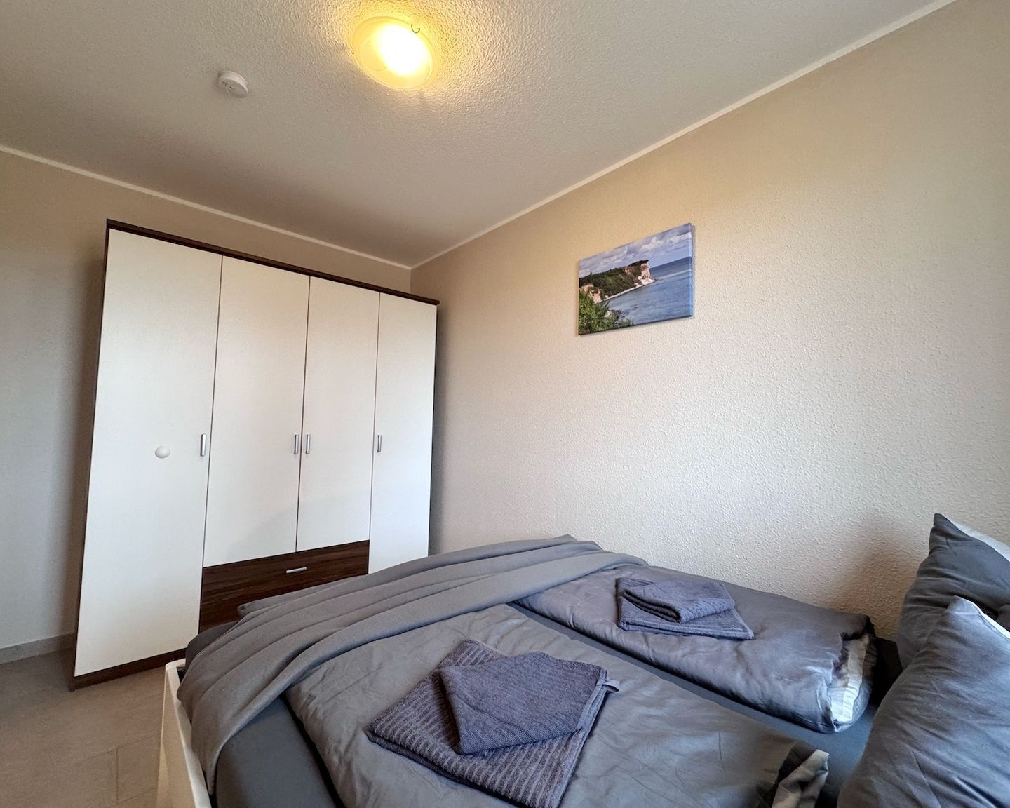Une chambre à coucher comprenant un lit, une armoire, un luminaire au plafond et un tableau accroché au mur.