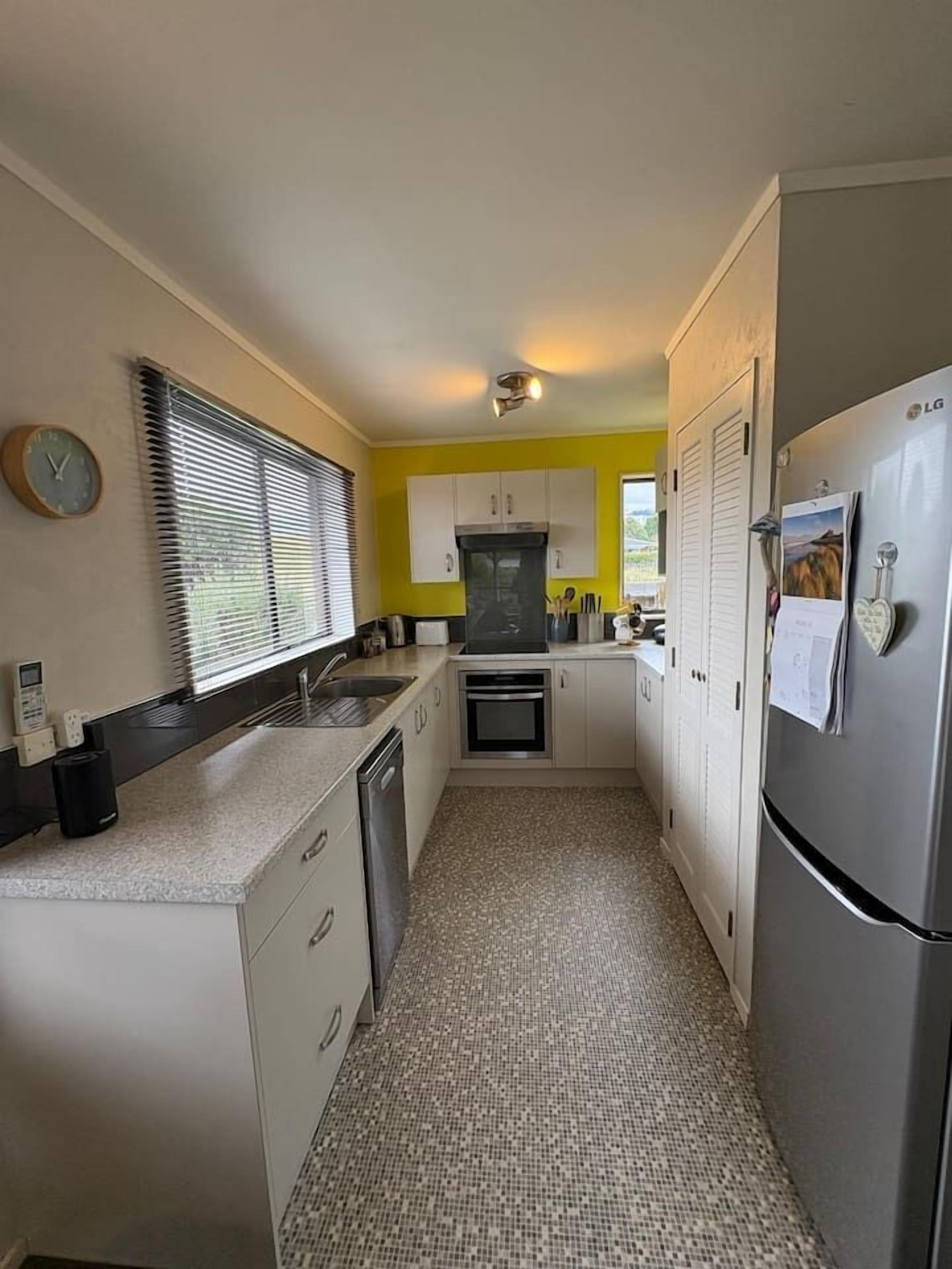 A compact kitchen with white cabinets, a stainless steel refrigerator, and a tiled floor.