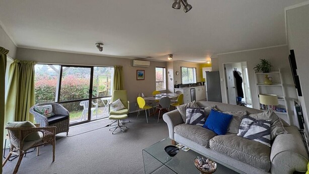 Een ruime woonkamer met een bank, stoelen, een eettafel en een keukenhoek.