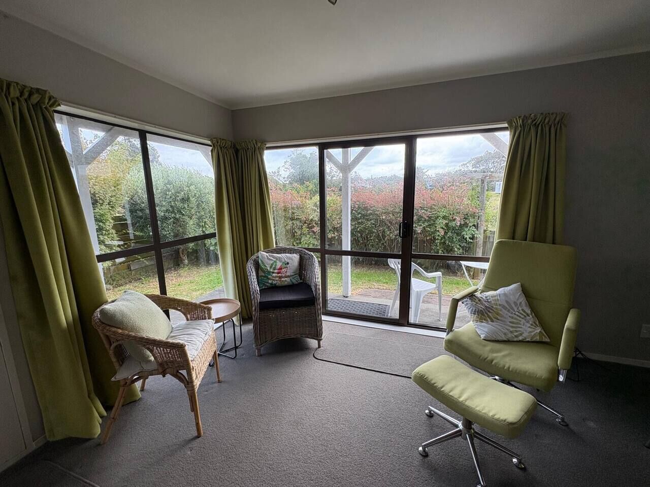 A room with large windows, a wicker chair, a cushioned armchair, and a small table.